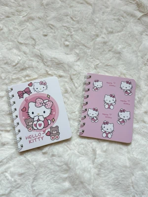 Hello Kitty spiralblock set - Två söta spiralblock med Hello Kitty-motiv. Ena blocket är vitt med rosa cirkel och nallebjörnar, det andra är ljusrosa med flera små Hello Kitty-figurer. Perfekta för anteckningar eller dagbok. Omslagen är i kartong och båda har rundade hörn.