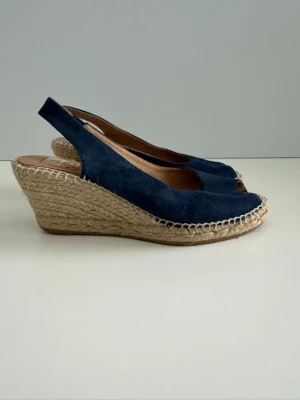 Marinblå kilklackade sandaler, 100% äkta mocka, 39 - Stilrena marinblå sandaler / espadrilles med öppen tå och kilklack i flätad jute från Kanna i storlek 39. Ovandelen är i 100% äkta mocka / skinn / läder och de har en öppen häl med rem. Bekvämaste skorna som är lika snygga till jeans som till klänning. Fint skick!!