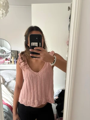 Ljusrosa stickad linnetopp - Supersöt ljusrosa stickad linnetopp med volangdetaljer vid axlarna och v-ringning. 