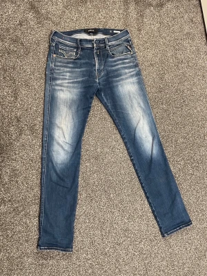 Replay Anbass Slim Fit Jeans – W31 L31 - Snygga blå slim fit jeans från Replay med coola slitningar och ljusa tvättade partier både fram och bak. Klassisk femficksmodell med dragkedja och knapp.  Tillverkade i bomull med stretch för extra komfort och perfekt passform. Riktigt snygga slitningar som ger ett trendigt, “archive” look. Pris 749kr! Storlek: W31 L31 Skick: Bra, välvårdade Perfekt för: Casual eller streetstyle                 