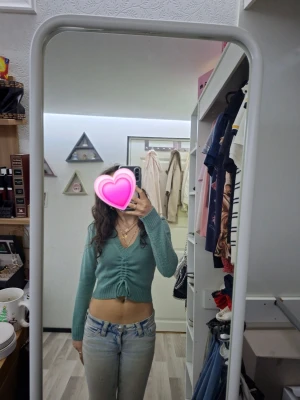 Grön cropped kofta med knyt - Tyrkås/Grön cropped kofta med långa ärmar och knytning framtill som ger en snygg rynkeffekt. Djup v-ringning och ribbade muddar vid ärmslut och nederkant. Perfekt att styla med jeans eller kjol för en cool look.