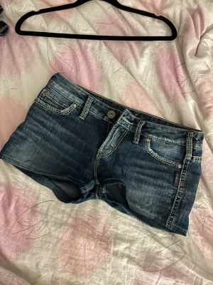 Blå jeansshort sop Silver Jeans - Snygga blå jeansshorts från Silver Jeans med slitna detaljer och kontrastsömmar. Storlek W27. 