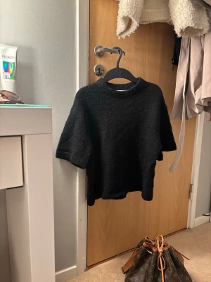 Svart stickad tröja Gina Tricot - Kort svart stickad tröja från Gina Tricot med rund halsringning och halvlånga ärmar. Tröjan har en enkel och stilren design, perfekt att matcha med både jeans och kjol. Materialet är mjukt och ger en mysig känsla.