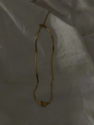 Guldigt halsband med fjärilshänge - Snyggt halsband i guldfärgad metall med platt kedja och ett litet fjärilshänge framtill. Perfekt accessoar för att lyfta din outfit med en trendig detalj. Justerbar längd med kedja baktill.