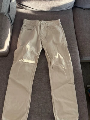 Beiga raka jeans från Zara - Säljer ett par beiga jeans från Zara med rak passform och klassisk femficksdesign. Jeansen har bälteshällor, knappgylf och är tillverkade i ett mjukt bomullstyg. Perfekta för en clean och stilren look.