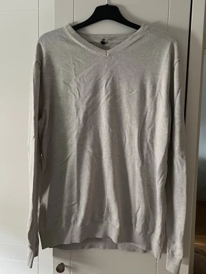 Ljusgrå V-ringad tröja - En enkel och stilren ljusgrå tröja med V-ringning och långa ärmar. Tröjan har ribbade muddar vid ärmslut och nederkant. Perfekt basplagg för lager på lager och funkar till det mesta.