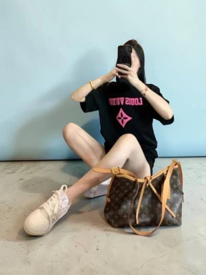 Iouis Vuitton T-shirt  - Exklusiv svart t-shirt med neonrosa 3D-logotyp Stilren t-shirt i högkvalitativ svart bomull med iögonfallande detaljer. Plagget har en centrerad logotyp på bröstet och ett större texttryck på ryggen, båda utförda i ett upphöjt, gummerat 3D-tryck i klarrosa neon. Den taktila effekten ger tröjan en modern och lyxig känsla. Färg: Svart med neonrosa detaljer. Design: Rundhalsad med korta ärmar och klassisk passform. Detalj: Markant 3D-textur på alla tryck.( Fast pris)