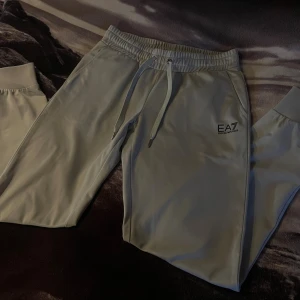 EA7  Emporio Armani Mjukisbyxor - Snygga mjukisbyxor från EA7 Emporio Armani med dragsko i midjan och elastisk resår. Byxorna har en stilren design med logga på vänster ben och raka ben. Perfekta för en chill och avslappnad stil.