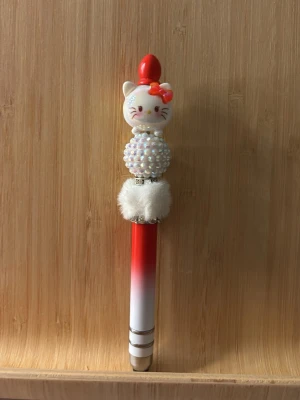 Söt kattpenna med pärlor och fluff - Unik bläckpenna med kattmotiv på toppen, dekorerad med vita pärlor och fluffig detalj. Pennan är röd och vit med silverfärgade ringar och har ett lock. Perfekt för dig som gillar gulliga och kreativa skrivsaker. Det är även en dutt penna  som du kan änvända på din iPad eller mobil.