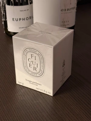 Diptyque Figuier doftljus 190g - Säljer ett exklusivt doftljus från Diptyque i doften Figuier. Ljuset kommer i en elegant vit kartong med klassisk Diptyque-design och väger 190g. Perfekt för att skapa en lyxig känsla hemma med en fräsch och grön doft av fikon.