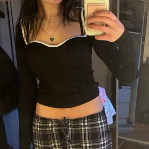 Svart croppad topp med vit kant - Trendig svart croppad topp med lång ärm och vit kontrastkant runt halsringningen. Toppen har en ribbad struktur och en snygg, figurnära passform som passar perfekt till höga byxor eller kjol. Från h&m