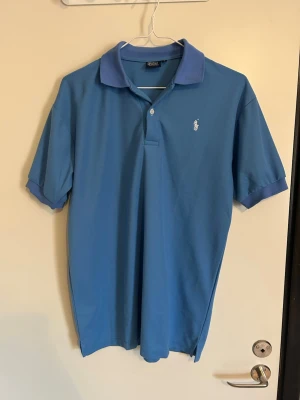 Blå pikétröja från Ralph Lauren - Ljusblå piké från Ralph Lauren. Vitt märke. Storlek L men passar M. 100% bomull