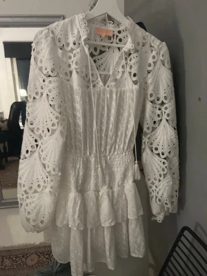 Vit spetsklänning med volanger - Superfin vit kortklänning med broderade spetsdetaljer och volanger. Perfekt för studenten🤍