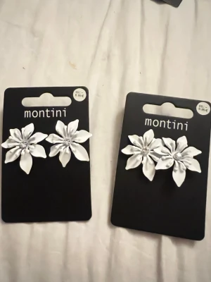 Vita blomörhängen från Montini - Säljer ett par vita örhängen från Montini i form av stora blommor. Örhängena har en snygg och detaljerad design med pärlliknande dekoration i mitten. Perfekta för dig som vill sticka ut med en unik accessoar. Säljer 1 för 69kr och 2 för 140kr 