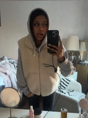 Beige teddyväst med dragkedja - Mysig beige teddyväst med dragkedja framtill och två fickor. Västen har en fluffig och mjuk textur, perfekt att slänga över en hoodie för en avslappnad look. 