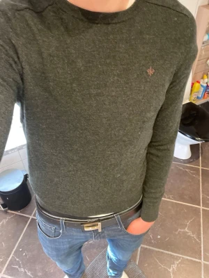 Mörkgrön stickad tröja från Morris - Mörkgrön stickad tröja från Morris med rund hals och smal passform. Tröjan har en liten broderad logga på bröstet och är gjord i mjukt systemsstickat material. Långa ärmar och stilren look. Den sitter som en S