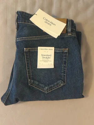 Calvin Klein raka blå jeans - Snygga blå jeans från Calvin Klein med rak passform och klassisk femficksdesign Kelly straight. Jeansen sopar golvet med soprena sömmar och har en tidlös look som passar till allt. Tillverkade i slitstarkt denimtyg.