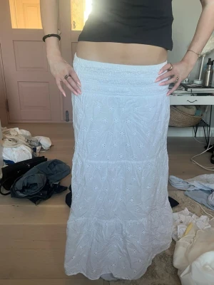 Vit långkjol med broderade detaljer - Säljer en super fin vit långkjol med broderade blommor och smock i midjan. Kjolen har volang längst ner och är gjord i ett lätt bomullstyg som passar perfekt till varma dagar. Super bra skick skriv för fler bilder eller frågor!!💕