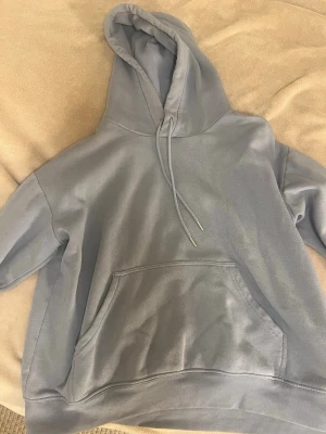 Ljusblå oversized hoodie - Säljer en ljusblå oversized hoodie med stor känguruficka framtill och dragsko i huvan. Hoodien har ribbade muddar vid ärmslut och nederkant. Perfekt för en chill och avslappnad stil. Materialet känns mjukt och bekvämt, troligen bomullsblandning.