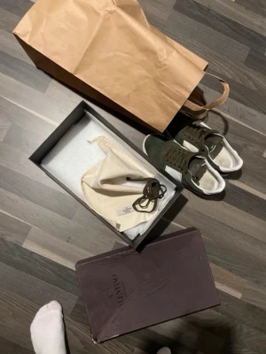 Valentino Garavani sneakers i mocka - Säljer ett par snygga Valentino Garavani sneakers i olivgrön mocka med vita skinnpaneler och coola nitar på sulan. Skorna har rund tå, snörning och klassisk låg profil. Perfekta för dig som vill ha en exklusiv touch till din outfit.