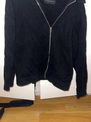 Svart ziptröja från Jack & Jones - Säljer en svart ziptröja från Jack & Jones med hel dragkedja framtill. Tröjan har lång ärm och är tillverkad i ett mjukt stickat material. Enkel och stilren design som passar till det mesta. Perfekt för lager på lager och chill vardagsstil.