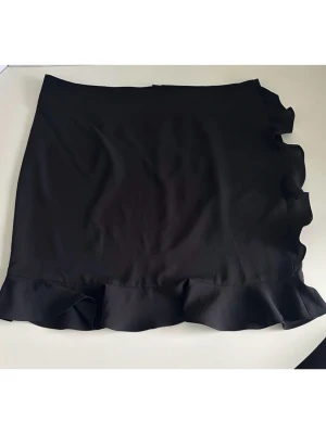 Svart kjol med volang från Daisy Grace - Otroligt fin svart kjol från Daisy Grace i storlek XL, modell Petit Belle Skirt. Vacker volang nedtill och på sidan, samt praktisk dragkedja bak. HELT NY med etikett. Nypris 800:-    (Skickas snabbt, men kan även hämtas i Stockholm om det är extra bråttom). 