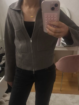 Åhléns kofta - Snygg kofta från Åhléns med rak passform, två stora bröstfickor och dragkedja framtill. Tröjan har en klassisk krage och är tillverkad i ett mjukt, stickat material som ger en clean och modern look.