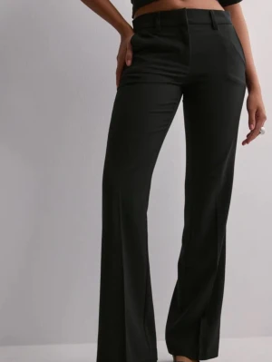 Svarta kostymbyxor med raka ben - Snygga svarta kostymbyxor med raka ben och hög midja. Byxorna har hällor för skärp, två sidofickor och stängs med dragkedja och knapp. Klassisk och stilren modell som passar till många olika looks.