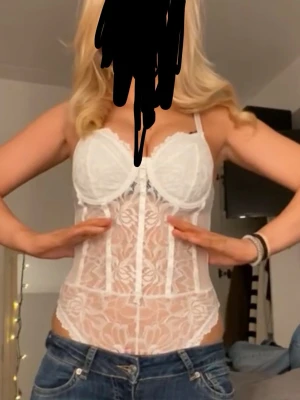 Vit spetskorsett med blommönster - Säljer en snygg vit korsett med blommigt spetsmönster och justerbara axelband. Den har byglar vid bysten för extra stöd och en genomskinlig mesh-design som ger en feminin look. Perfekt att styla med jeans eller kjol.