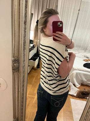 Vit stickad tröja med svarta ränder - Snygg vit stickad tröja med svarta horisontella ränder och korta ärmar. Tröjan har en avslappnad passform och ribbstickad nederkant. Perfekt för en trendig och bekväm look. HELTOANVÄND