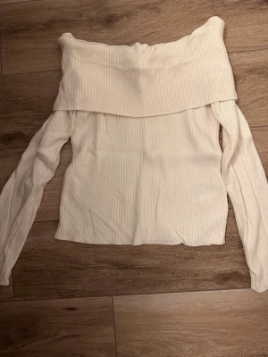 Offshoulder ribbad topp från H&M - Trendig offshoulder topp från H&M i ljus beige färg. Toppen är ribbad och har långa ärmar samt en bred, vikt kant upptill som ger en snygg look. Perfekt att styla med jeans eller kjol för en chic outfit.