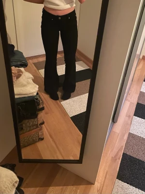 Svarta bootcut jeans - Säljer ett par svarta bootcut jeans med låg midja och klassisk femficksdesign. Jeansen har utsvängda ben och sitter tight över höfterna. 