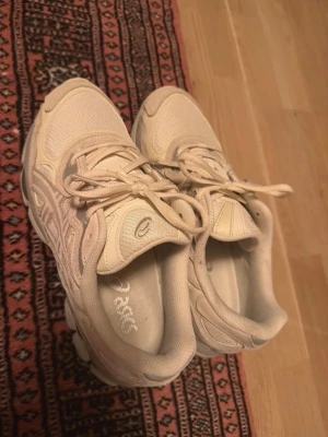 Beige sneakers från Asics - Snygga beige sneakers från Asics med klassisk mesh och syntetmaterial. Skorna har låga skaft, tydliga Asics-loggor på sidan och på plösen samt en chunky sula för extra streetkänsla. Perfekta för dig som gillar stilrena och neutrala färger.
