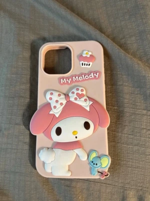 My Melody rosa mobilskal i silikon - Sött rosa mobilskal till iPhone 13 Pro Max med 3D-design av My Melody, cupcake och mus. Tillverkat i mjukt silikon med detaljer i vitt, rosa och blått. Perfekt för dig som gillar kawaii och vill ha ett unikt skal med gulliga figurer.
