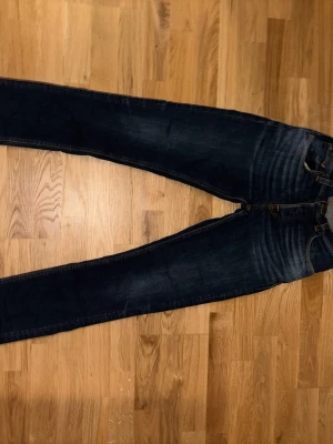 Mörkblå jeans från Nudie Jeans - Säljer ett par mörkblå jeans från Nudie Jeans med klassisk grim tim passform och snygga slitningar framtill. Jeansen har rak/ lite slimmad passform. Inga hål eller liknande, allmänt jävligt bra skick. 