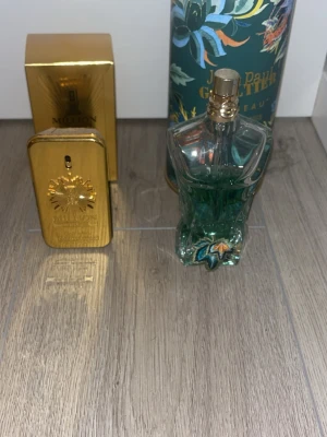 Paco Rabanne 1 Million & Jean Paul Gaultier Le Male - Två ikoniska herrparfymer: Paco Rabanne 1 Million i en guldig, rektangulär metallflaska med matchande förpackning och Jean Paul Gaultier Le Male i en turkos, kroppformad glasflaska med dekorativ förpackning. Båda dofterna är populära och har unika, lyxiga designer. Ungefär hälften kvar i båda 