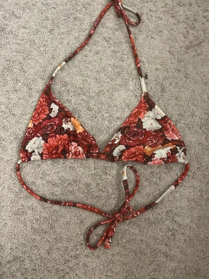 Blommig bikiniöverdel från NA-KD - Snygg trekantsbikini från NA-KD med blommigt mönster i rött, vitt och orange. Klassisk modell med knyt i nacke och rygg, perfekt för sommaren. Materialet känns mjukt och följsamt mot huden.