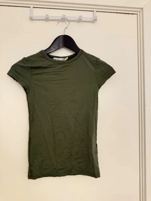 Olivgrön basic t-shirt - En enkel olivgrön t-shirt med rund hals och korta ärmar. Perfekt att matcha med jeans eller shorts för en avslappnad stil. Tillverkad i mjuk bomull för skön känsla hela dagen.