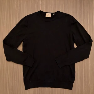 Marinblå stickad tröja från Bläck - Klassisk marinblå stickad tröja från Bläck med rund halsringning och långa ärmar. Tröjan har en enkel och stilren design med ribbade muddar vid ärmslut och nederkant. Perfekt som lager på lager. Det ser ut som den är svart på bilden men den är marinblå/mörkblå egentligen.  Nypriset är 700kr