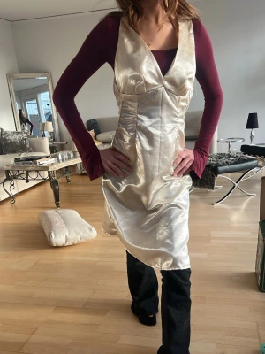 Champagnefärgad omlottklänning i satin - handgjord Snygg champagnefärgad omlottklänning i glansigt satinmaterial. Klänningen har v-ringning, markerad midja och slits i sidan för en trendig look. Perfekt för dig som vill sticka ut med en elegant och modern stil. har ett litet hål men det är inte märkbart alls. priset kan diskuteras!