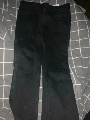 Svarta jeans från wrangler - Säljer ett par svarta jeans från wrangler  med klassisk femficksmodell och raka ben. Jeansen har bälteshällor och dragkedjegylf. Perfekta för dig som gillar en enkel och stilren look.