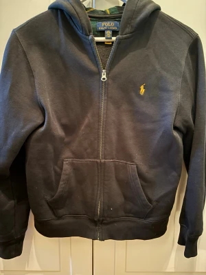 Svart hoodie från Polo Ralph Lauren - Säljer en väldigt snygg och unik Ralph Lauren hoodie! Den är svart med en flannel hoodie. Storleken är 14/16 och är som en XS! Fick den i julklapp förra året och har använt den nån gång ibland. Skriv till mig vid minsta fundering! /Gustav 😁