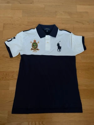 Piké från Polo Ralph Lauren - Stilren piké från Polo Ralph Lauren i marinblått och vitt. Toppen har klassisk krage, korta ärmar och broderade detaljer på bröstet och ärmen. Helt ny använd en gång. Storleken motsvarar/passar S i herr. Tveka inte på att höra av dig vid frågor! Nypris runt 1500 kr. 