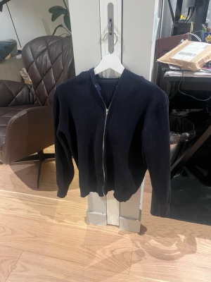 Mörkblå ziptröja med huva - Säljer en mörkblå stickad ziptröja med huva. Tröjan har långa ärmar, ribbade muddar och dragkedja framtill. Perfekt för dig som gillar en enkel och stilren look.