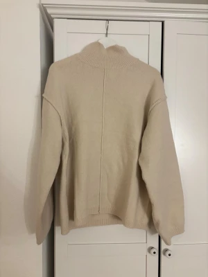 Beige stickad polotröja M - Säljer en beige stickad polotröja i storlek M. Tröjan har en hög ribbad krage, raka ärmar och en avslappnad passform. Materialet är mjukt och tröjan har en diskret söm mitt bak. Perfekt för lager på lager och enkel att styla.