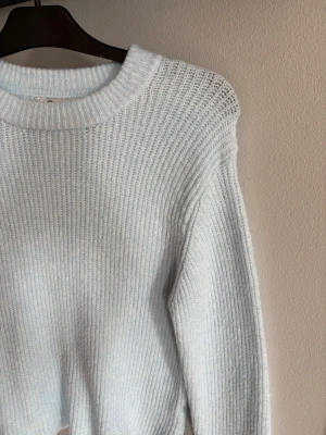 Ljusblå stickad tröja med rund hals - En ljusblå stickad tröja med ribbad struktur och rund halsringning. Tröjan har långa ärmar och är tillverkad i ett mjukt material som ger en skön känsla. 