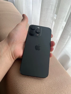 Svart iPhone 16 pro Max 256 G - Snygg svart iPhone med stilren design och trippelkamera på baksidan. Mobilen har en matt finish och rundade hörn, med Apples logga centralt placerad. Skärmen är stor och täcker hela framsidan, perfekt för streaming och sociala medier.