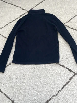 Svart ribbad tröja med halvzip - Svart långärmad ribbad tröja med halvzip och hög krage. Perfekt för lager-på-lager och enkel att matcha med jeans eller kjol. Materialet är mjukt och stretchigt, vilket gör den bekväm att bära hela dagen.