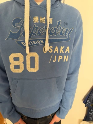 Superdry hoodie  - Blå superdry hoodie, fet passform storlek M har tyvär ett litet hål vid vänstra armen längst ut 