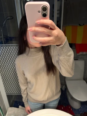 Beige stickad tröja med hög krage - En enkel och stilren beige stickad tröja med hög krage och långa ärmar. Tröjan har ribbade muddar vid ärmslut och nederkant, perfekt för att hålla värmen. Passar bra till jeans och har en avslappnad passform. Tröjan är lite nopprig och man kan schystera kragen. Det finns ingen lapp men skulle säga att de passar ungefär storlek S🫶.